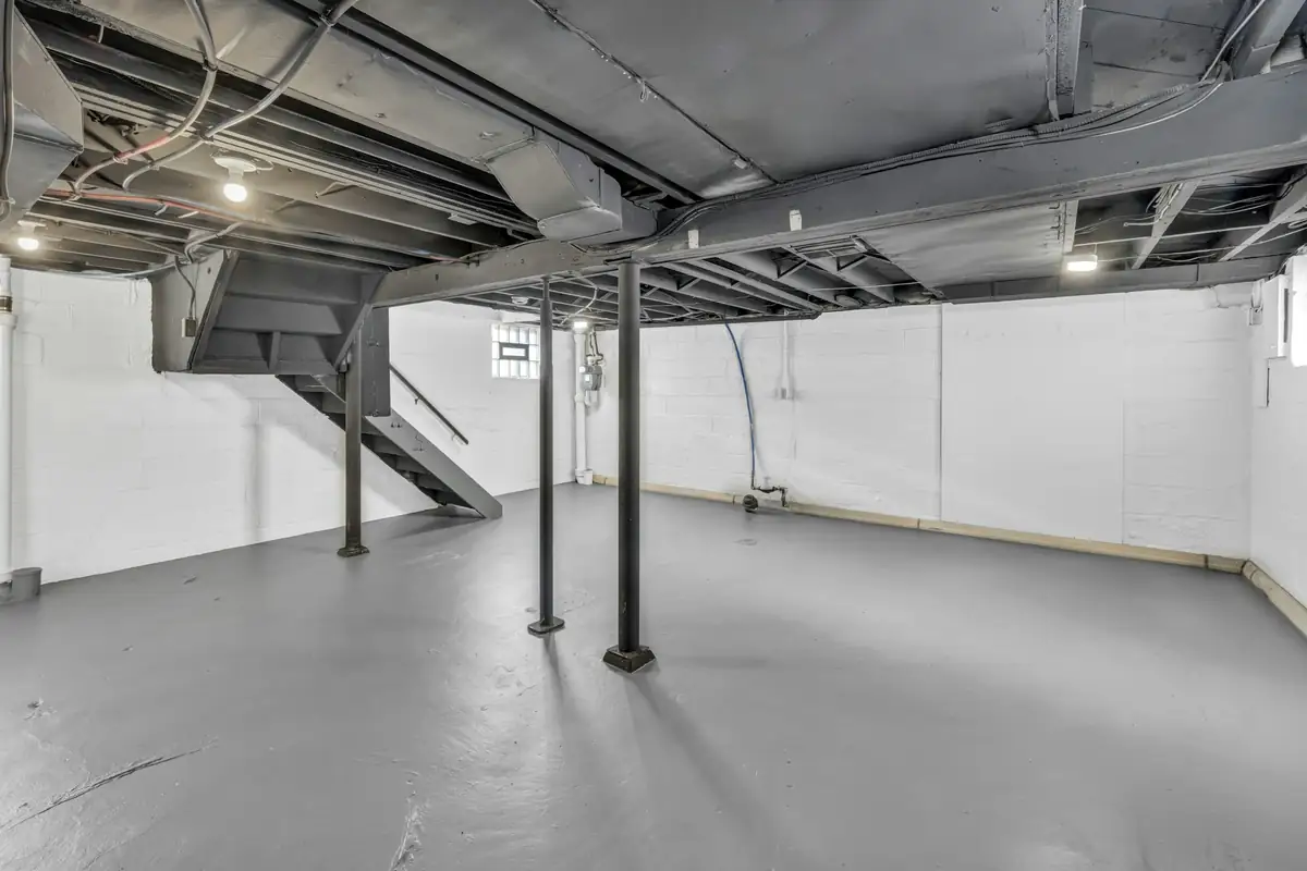Sous-sol vide aux murs blancs, sol peint gris, poteaux et solives apparentes