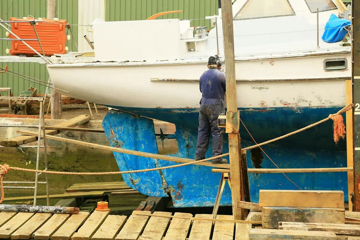 Voilier sur ber au chantier, un homme travaille sur la coque bleue écaillée
