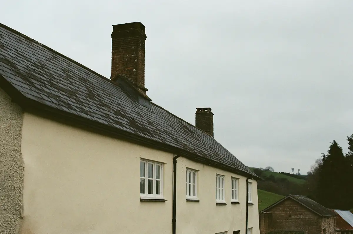 Maison enduite couleur crème sous un toit d'ardoise sombre et ses cheminées
