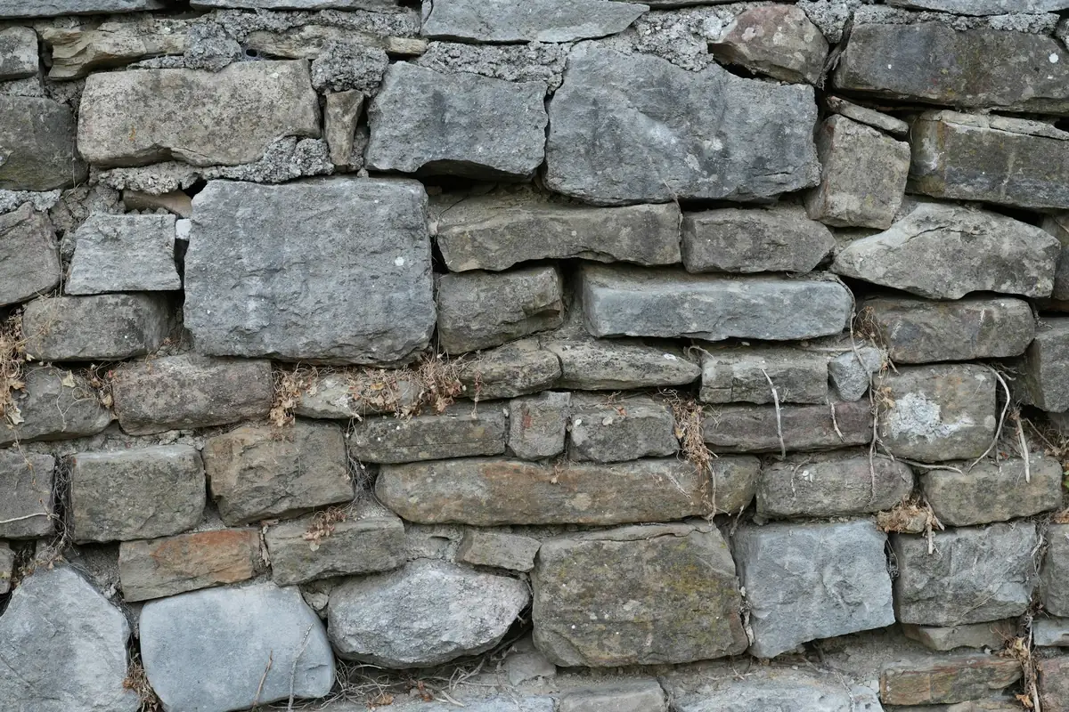 Mur de pierres grises empilées, assises irrégulières et joints garnis