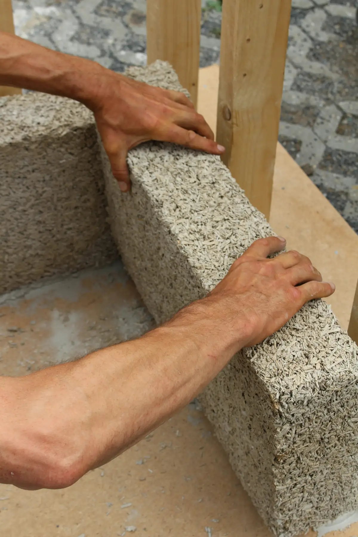 Mains posant un bloc de béton gris sur un mur en cours de montage