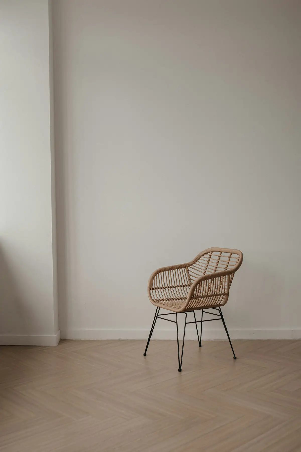 Parquet clair posé en chevrons dans une pièce aux murs blancs, fauteuil en rotin