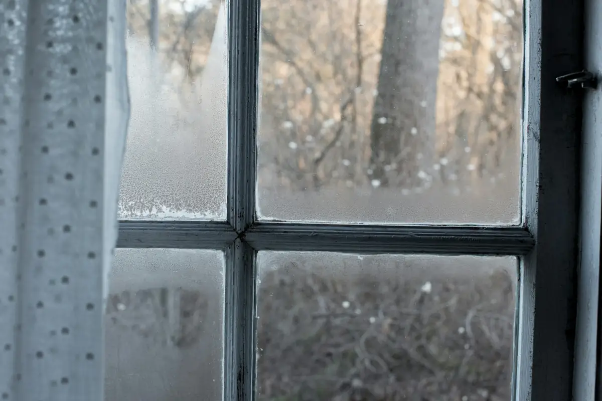 Fenêtre à petits bois couverte de buée, rideau voilage sur le côté